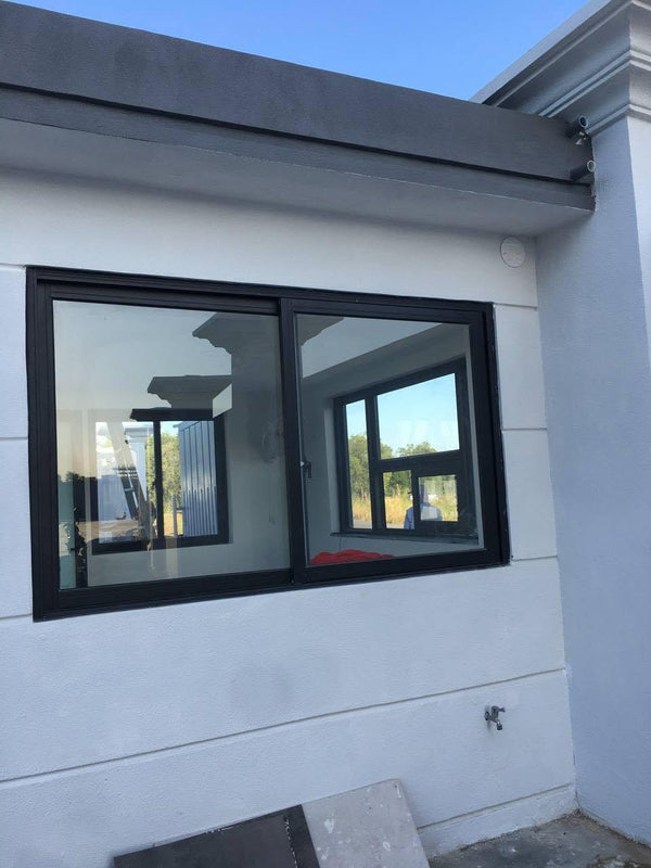Black aluminum double sliding window installed on the exterior wall of a modern house with white siding under a dark gray roof overhang.