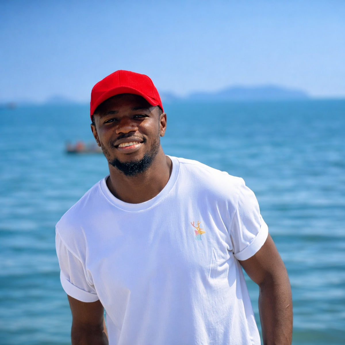 Man wearing a red cap and white t-shirt standing by the ocean