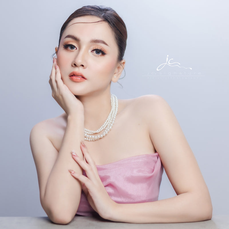 Woman wearing a pink strapless dress and pearl necklace against a light gray background