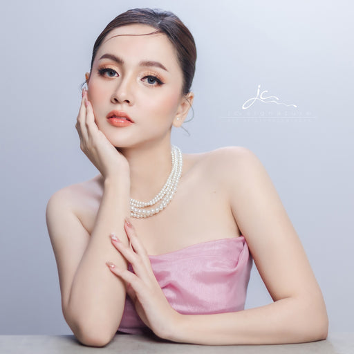 Woman wearing a pink strapless dress and pearl necklace against a light gray background