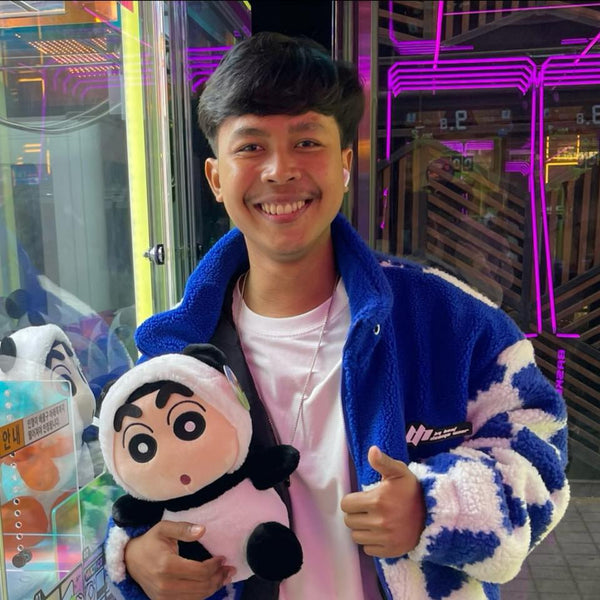 Person holding a plush toy in front of a claw machine with neon lights in the background