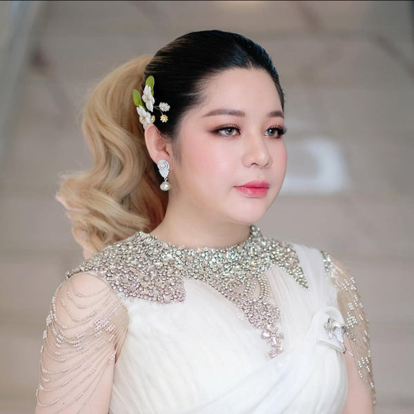 Woman in a white dress with embellishments and floral hair accessory against a neutral background