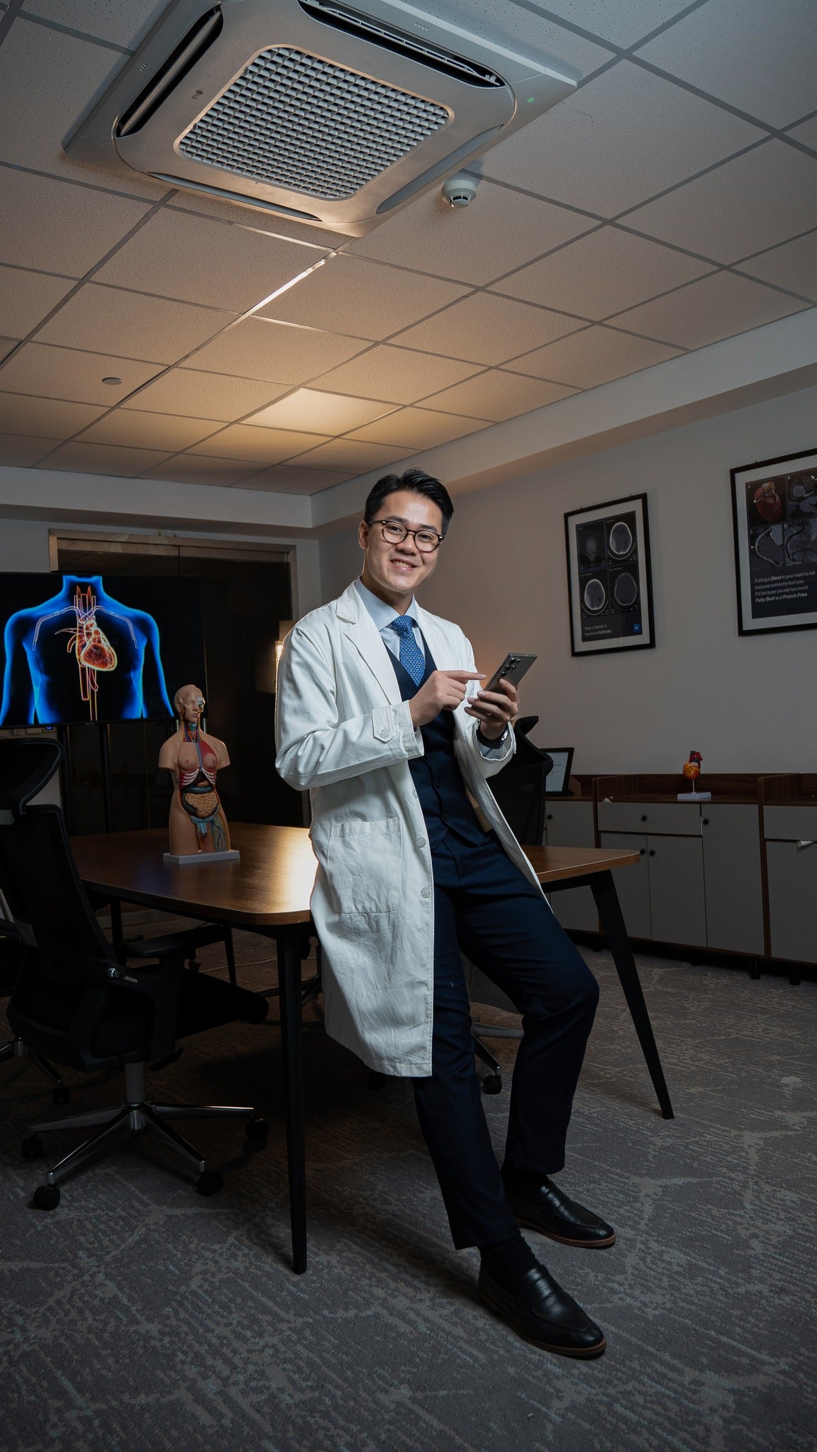 Doctor in a white coat holding a smartphone in an office setting.