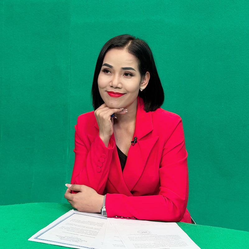 Woman in a red blazer sitting at a table with papers against a green background