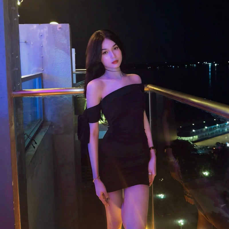 Woman in a black dress standing on a balcony at night with city lights in the background