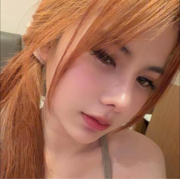 Close-up of a person with red hair tied back, wearing a gray top.