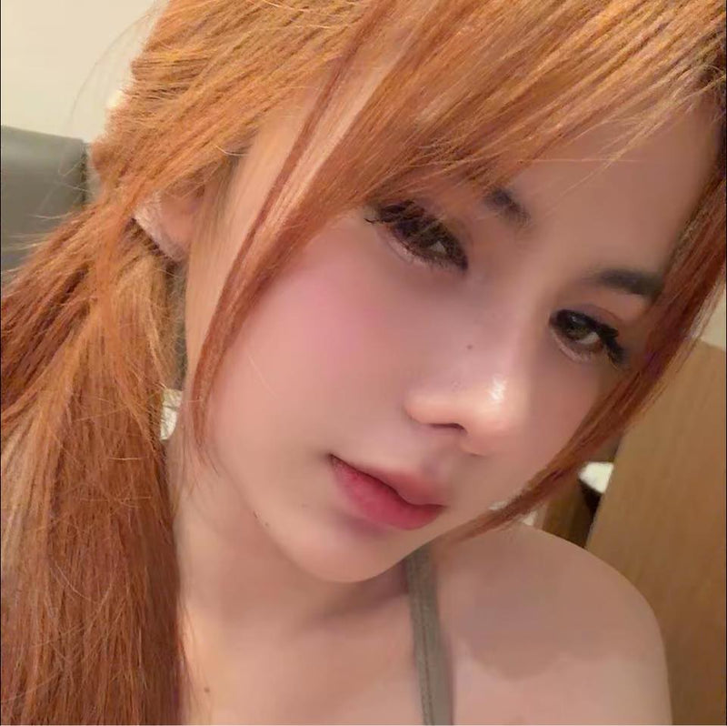 Close-up of a person with red hair tied back, wearing a gray top.