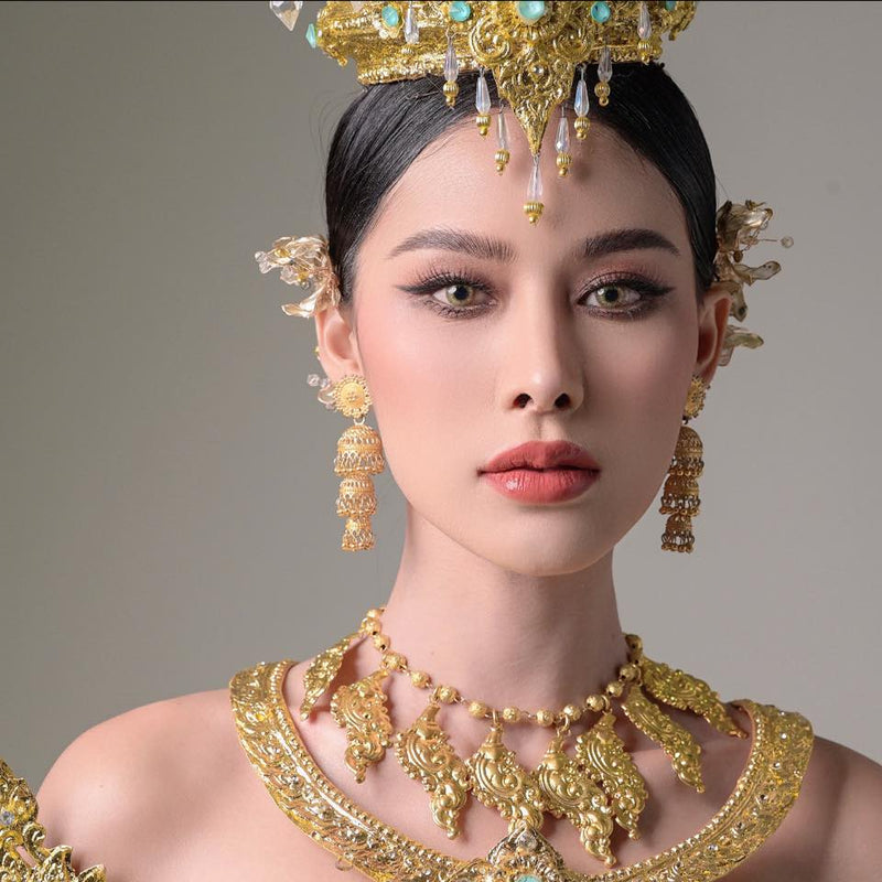 Woman wearing elaborate gold jewelry and a headpiece against a neutral background