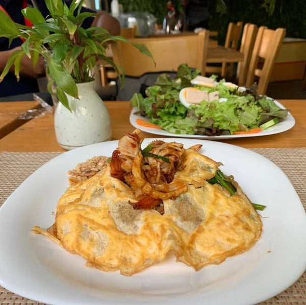 Two plates of food on a table with a salad in the background