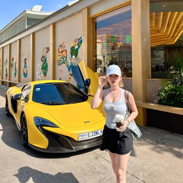 Woman standing next to a yellow sports car with open door, holding a coffee cup.