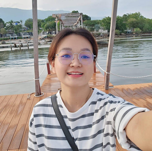 Person taking a selfie on a wooden dock by a body of water with mountains in the background.