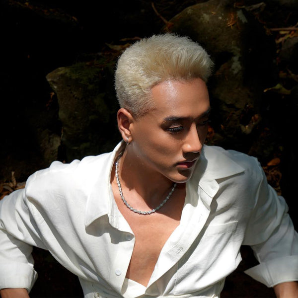 Person with platinum blonde hair wearing a white shirt and necklace in a natural setting