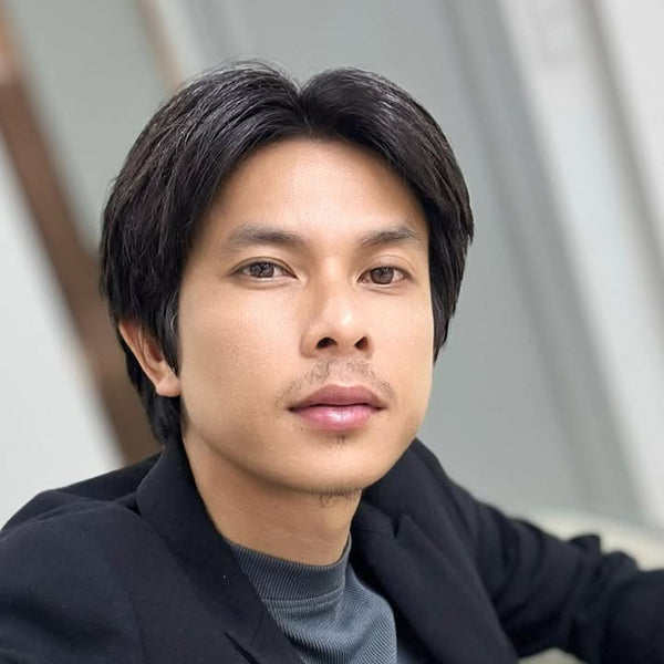 Man wearing a dark jacket over a gray sweater against a neutral background