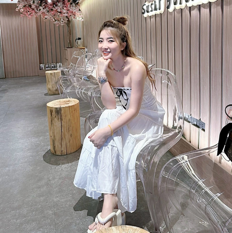 Woman in a white dress sitting on a transparent chair in a modern interior setting.
