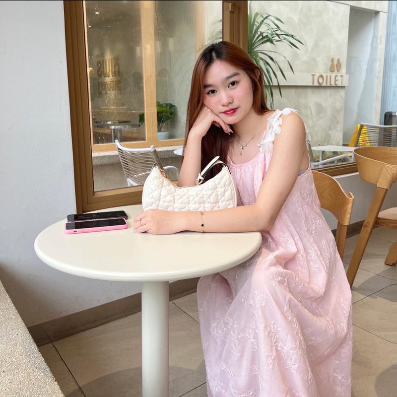 Woman in a pink dress sitting at a table with a white handbag and phone in a cafe.