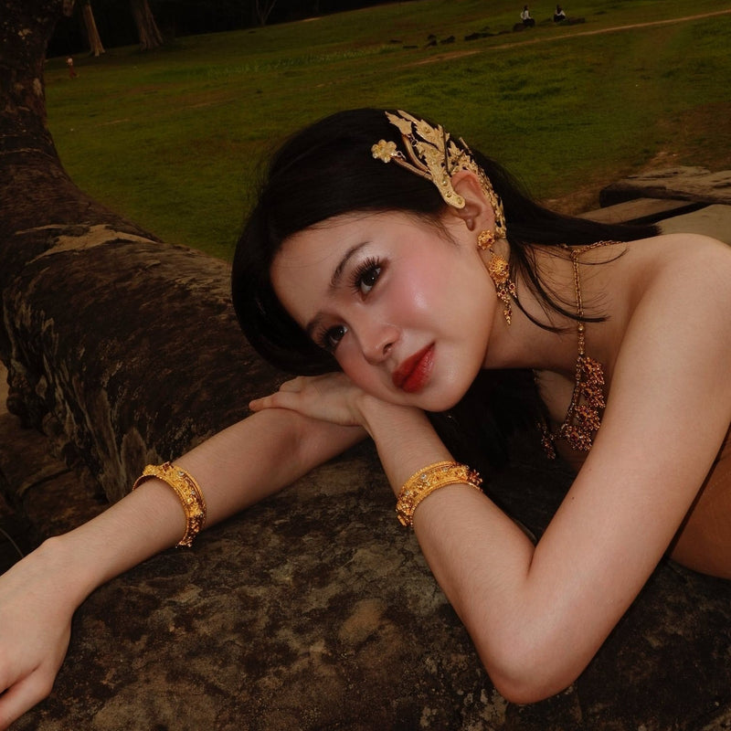 Woman wearing gold jewelry and traditional attire in a natural setting