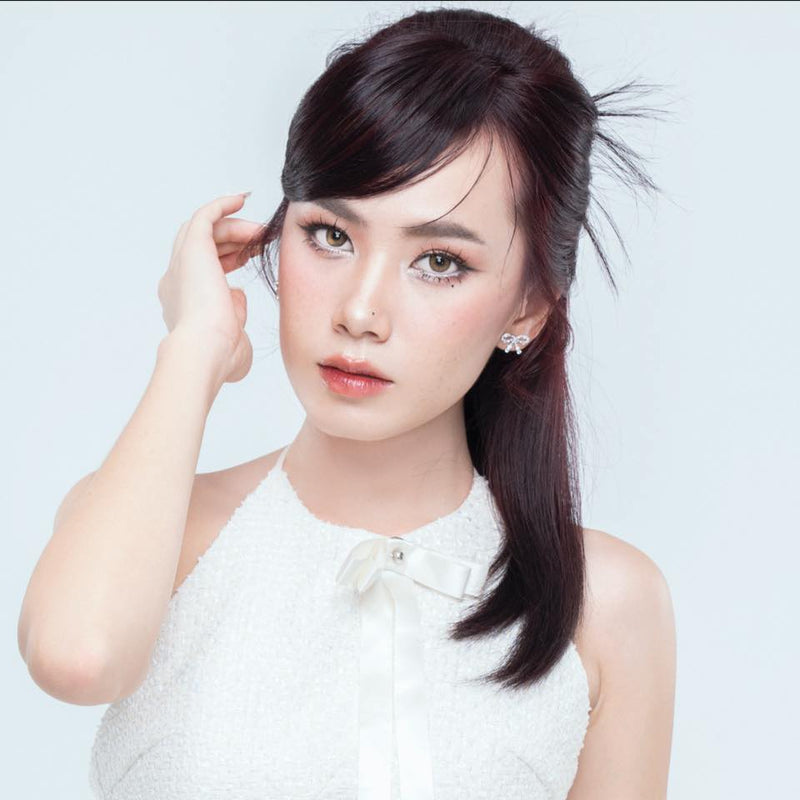 Woman with a ponytail wearing a white top against a light blue background