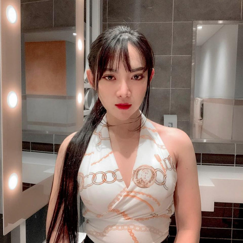 Woman in a white dress with orange patterns standing in a bathroom.