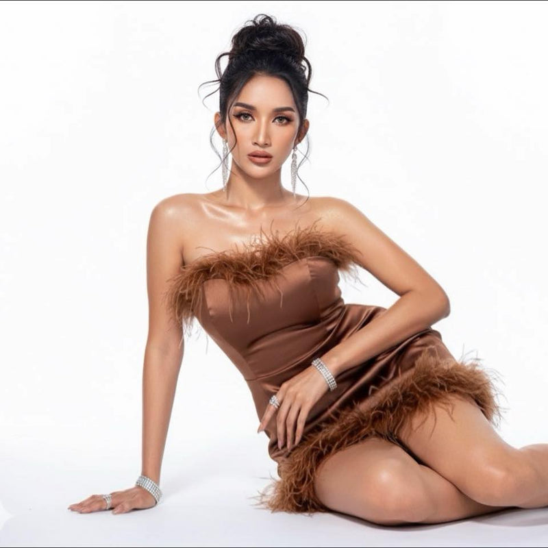 Woman wearing a brown strapless dress with feather details on a white background