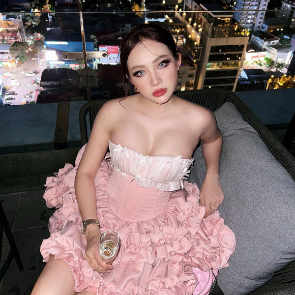 Woman in a pink dress sitting on a rooftop with city lights in the background
