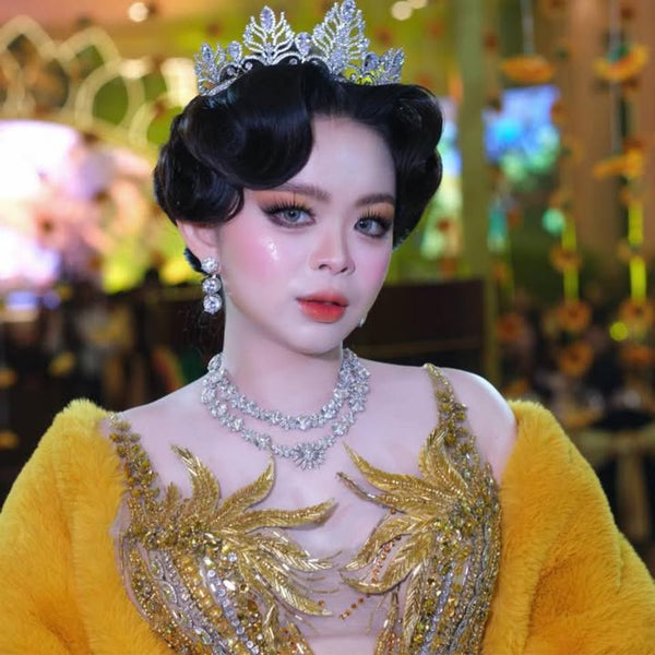 Person wearing a yellow embroidered outfit with a tiara and jewelry in a blurred indoor setting