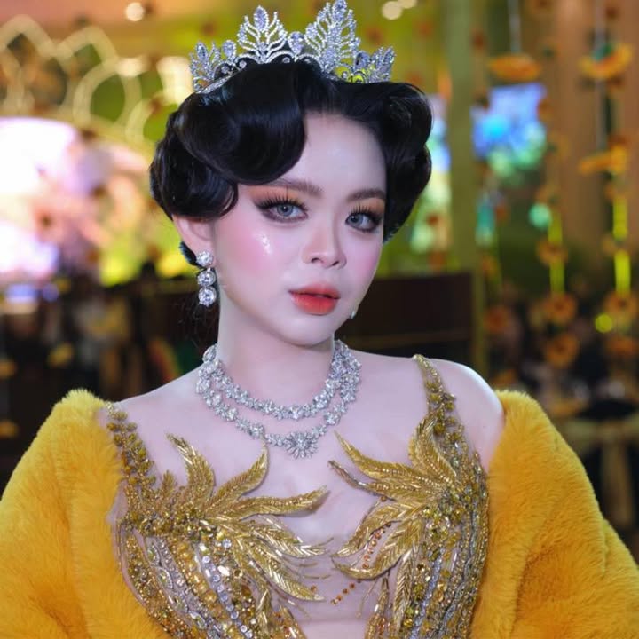 Person wearing a yellow embroidered outfit with a tiara and jewelry in a blurred indoor setting