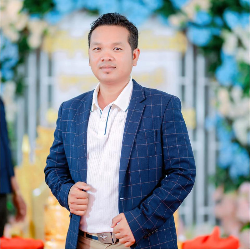 Man in a blue checkered blazer standing in front of decorative floral arrangements.