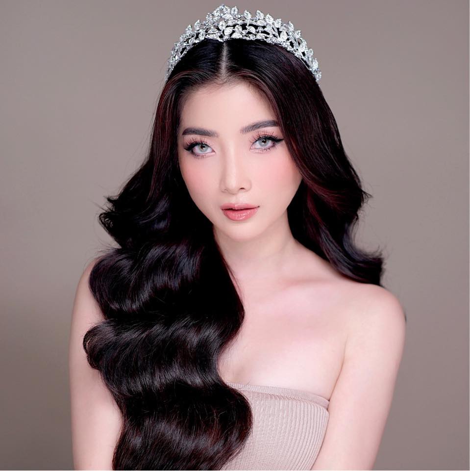 Woman with long wavy hair wearing a tiara against a plain background