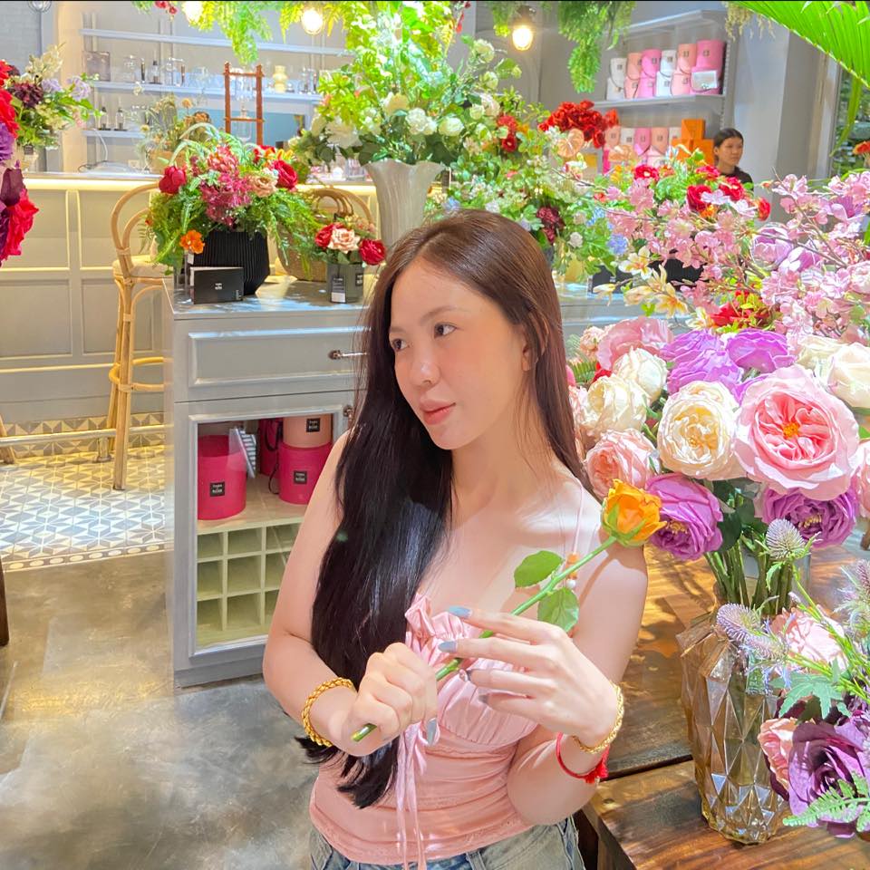 Woman holding flowers in a floral shop with various flower arrangements around her.