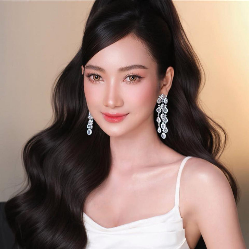 Woman with long dark hair wearing large earrings against a beige background