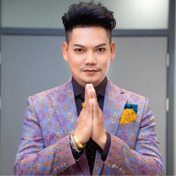 Man in a colorful suit with a yellow flower pin, standing against a neutral background