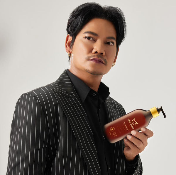 Man in a black pinstripe suit holding a bottle against a gray background