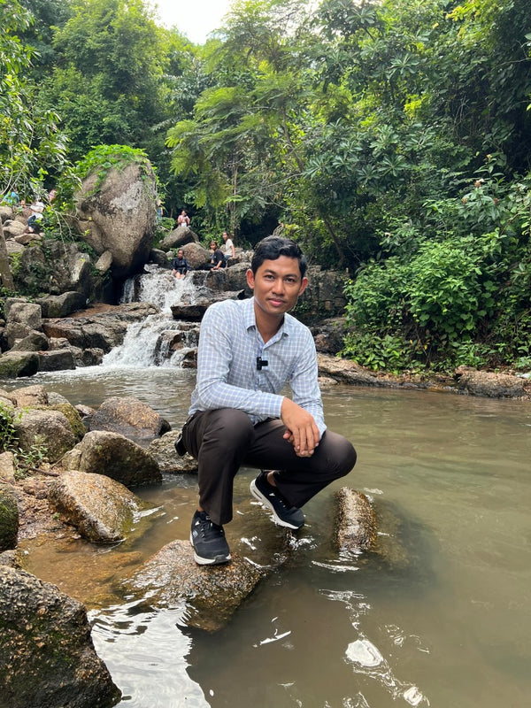 Man sitting by a small waterfall in a lush green forest