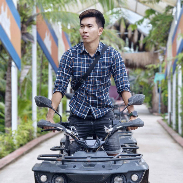 Man standing on a large toy truck in an outdoor setting with plants and colorful structures.