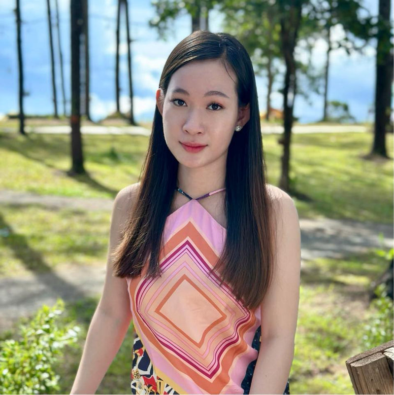 Woman in a colorful dress standing outdoors with trees and grass in the background