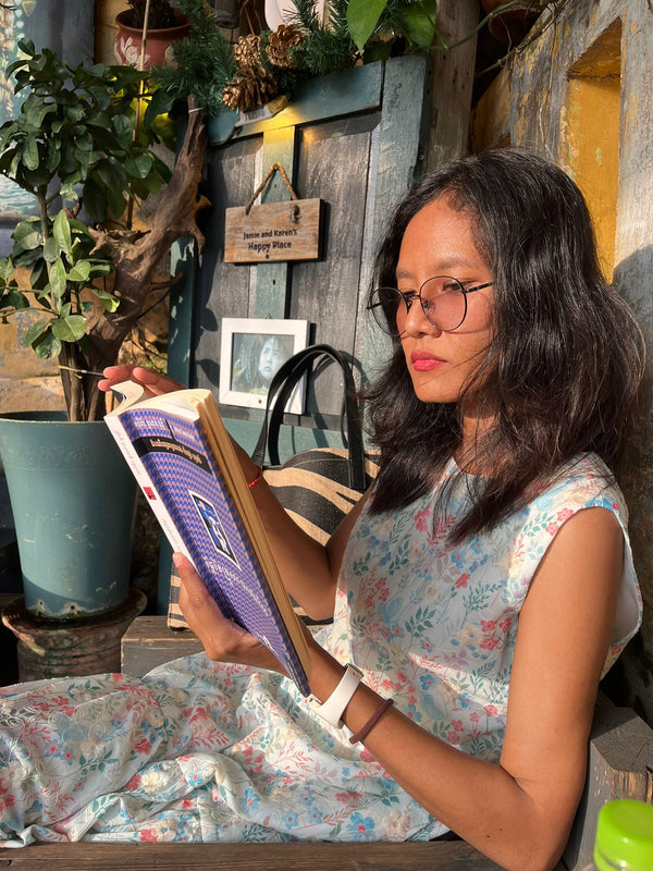 Woman reading a book in a cozy indoor setting with plants and wooden decor.