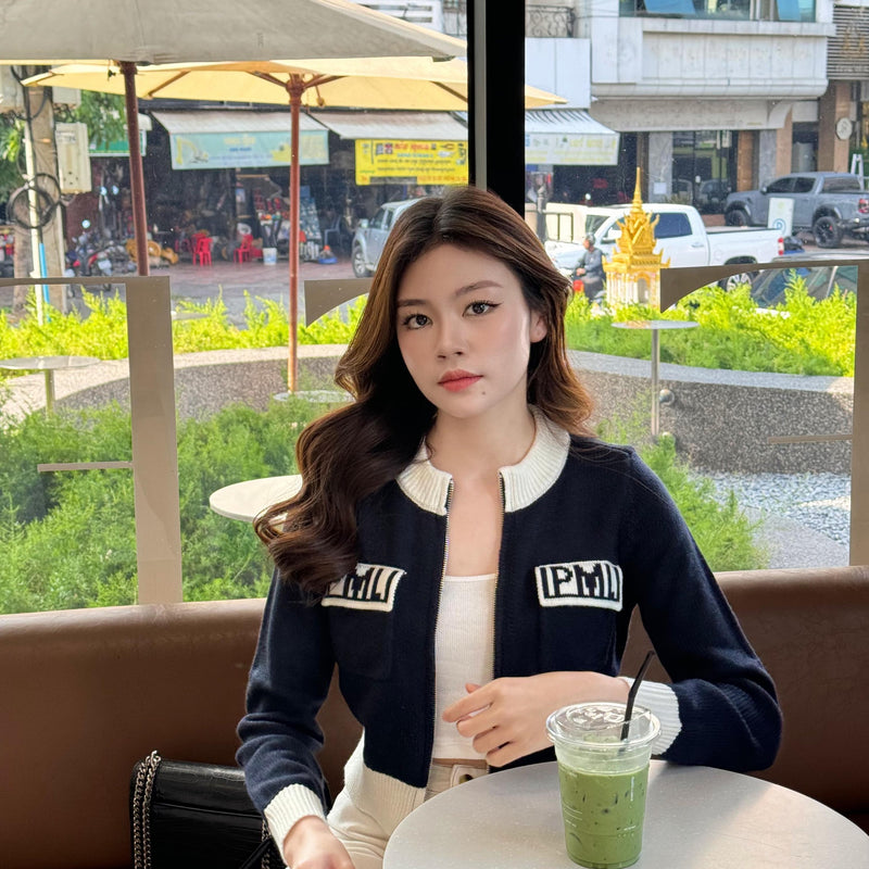 Woman sitting at a cafe with a drink, wearing a navy cardigan with 'IPMI' branding.