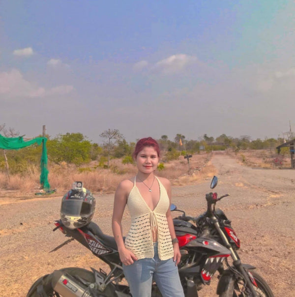 Woman standing next to a motorcycle on a desert road with a clear sky.