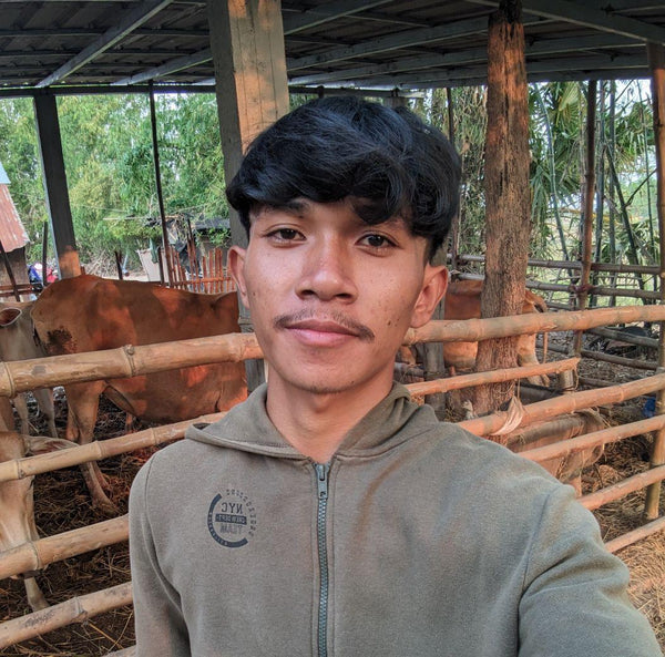 Person wearing a green hoodie in a rustic setting with wooden structures and animals.
