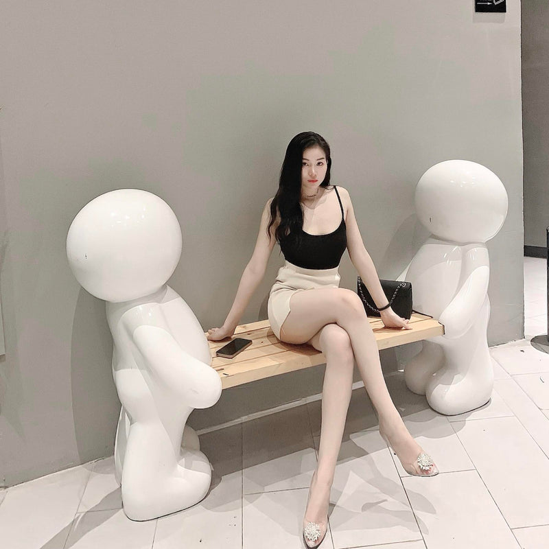 Woman sitting on a bench between two white abstract sculptures in a modern interior setting.