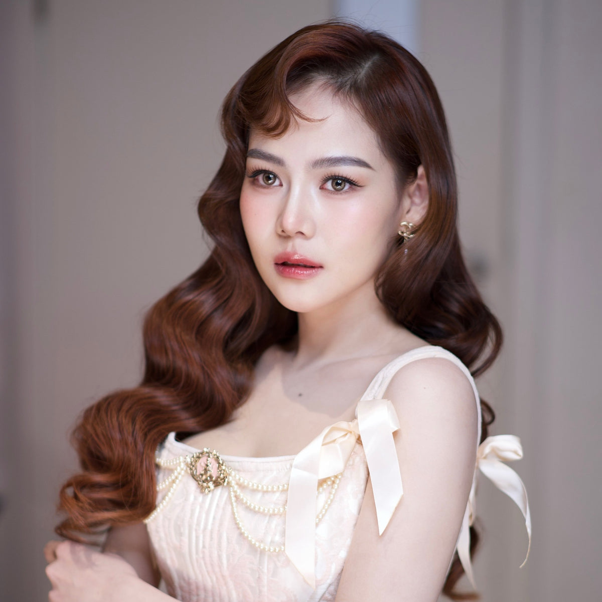 Woman with styled hair wearing a light-colored top with decorative elements.