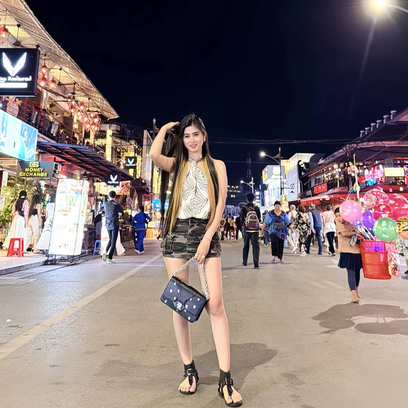 Woman posing on a street at night with colorful lights and people in the background