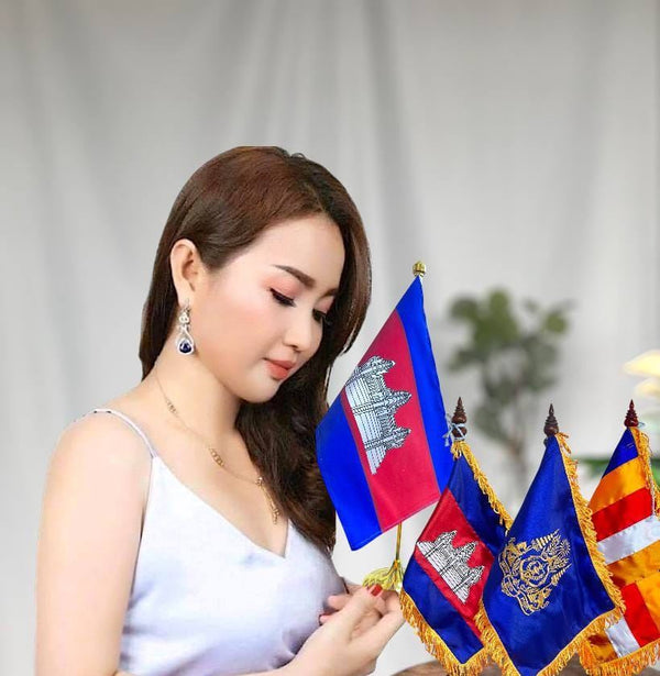 Woman holding a set of flags, including the Cambodian flag, against a neutral background.