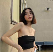 Woman wearing a black strapless top against a beige wall.